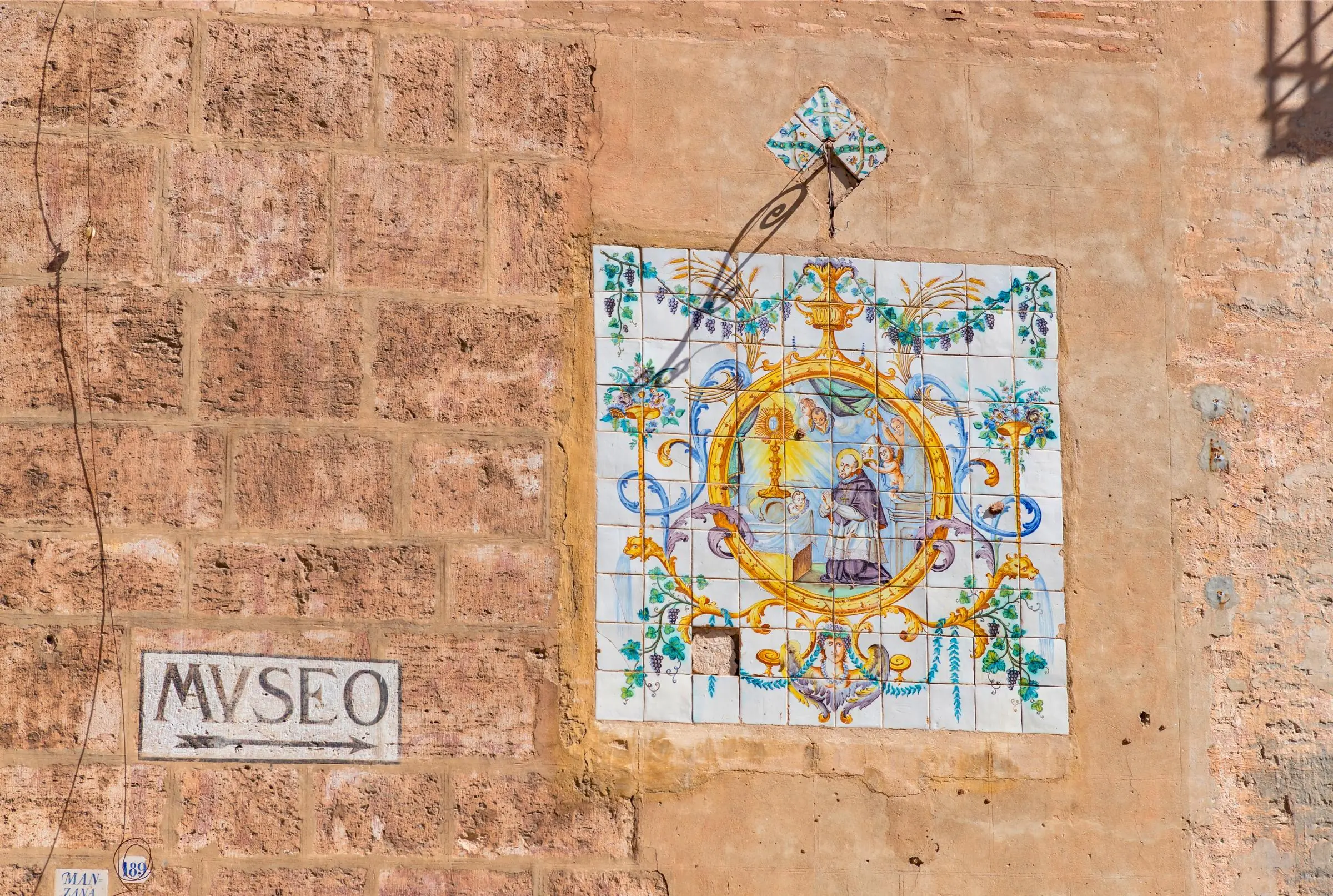 A ceramic tile mural and a painted stone sign pointing towards the museum entrance at El Patriarca