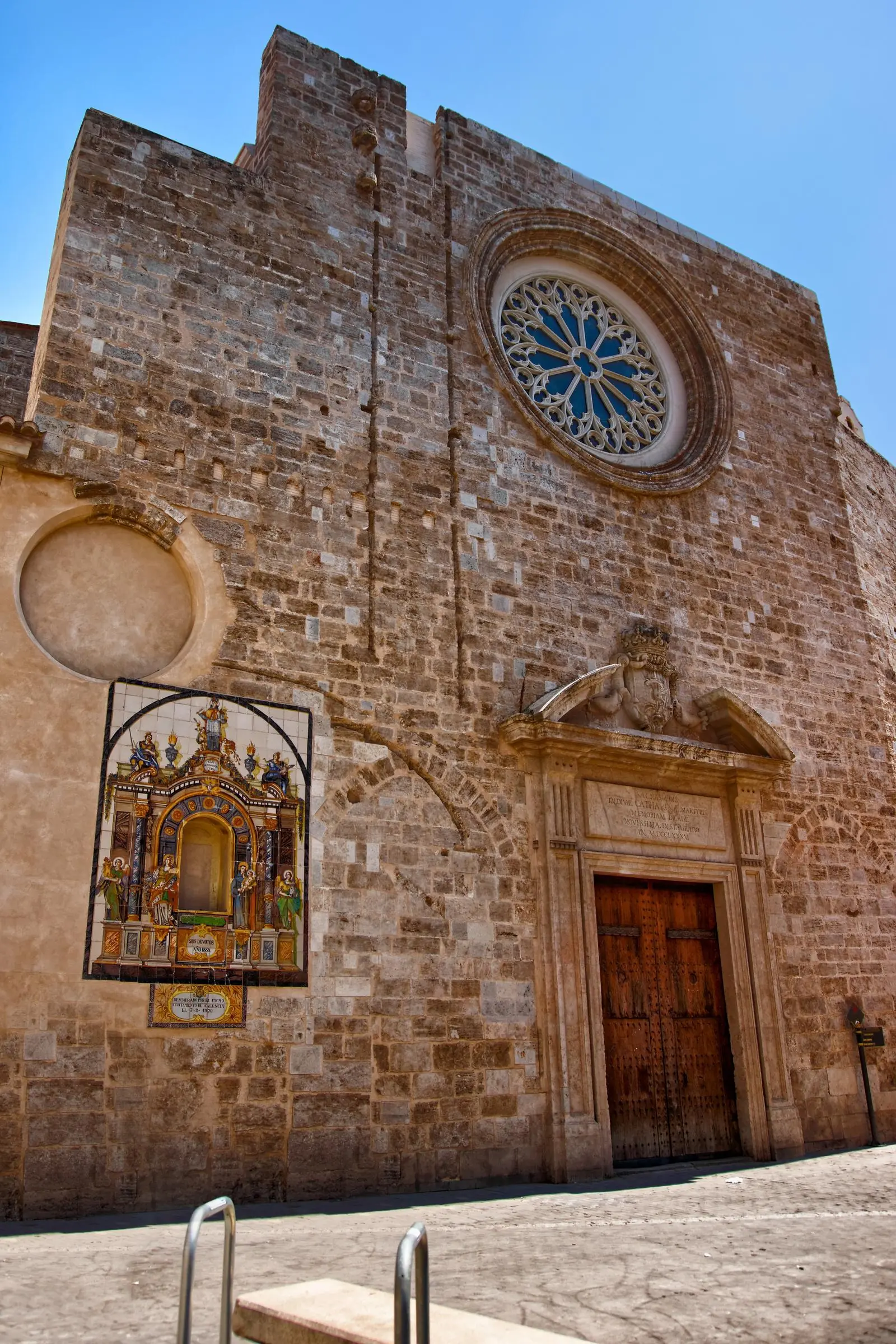 The stone facade of Santa Catalina featuring a Gothic rose window and historic painted tile mural